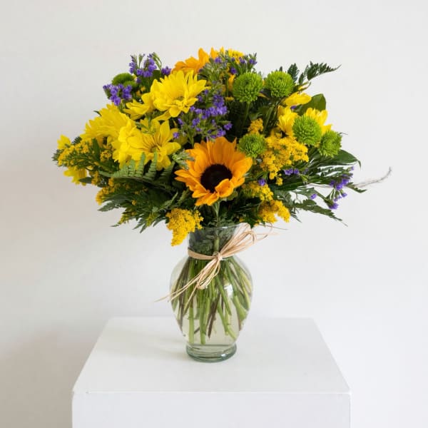 Yellow and purple mixed bouquet in a clear glass vase with a raffia bow