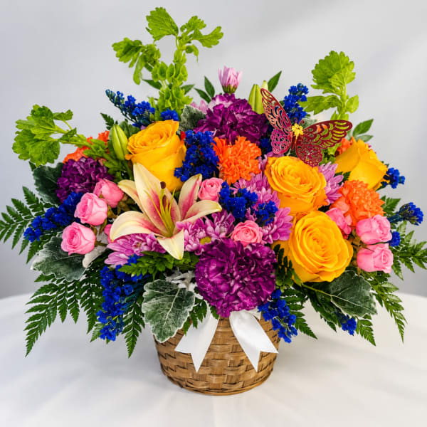 Colorful mixed flower arrangement in a woven basket with a white ribbon