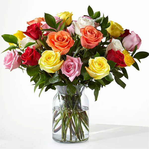 Mixed roses in pink, yellow, red, and peach arranged in a clear glass vase.