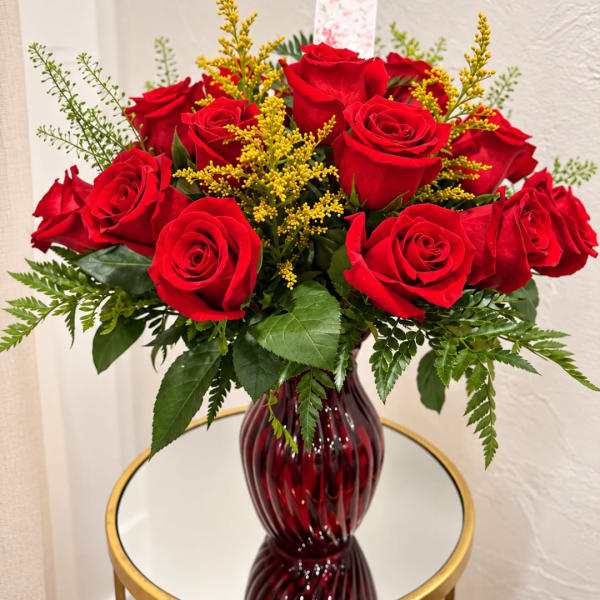 Red roses arranged in a burgundy glass vase with yellow filler flowers