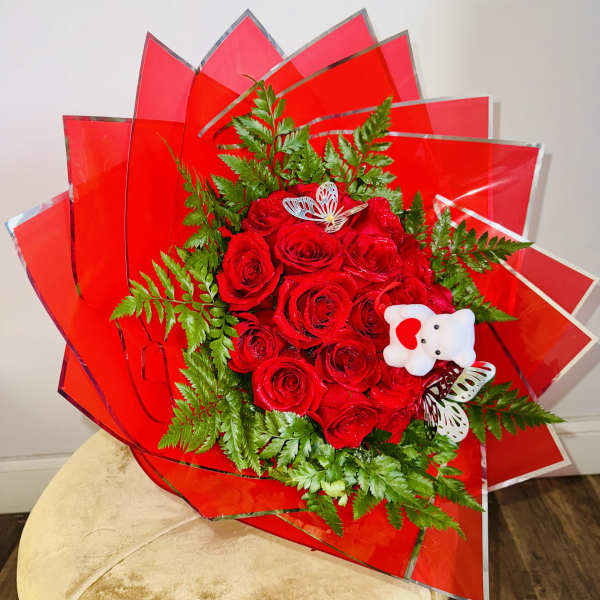 Red rose bouquet with green fern accents and a small teddy bear