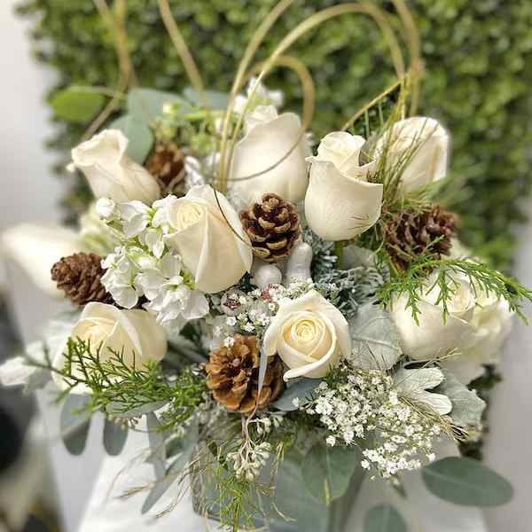 White rose arrangement with pinecones in a square vase against a green textured backdrop