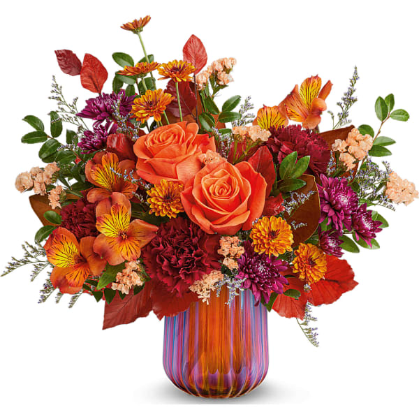 Orange roses and mixed fall flowers in a striped glass vase
