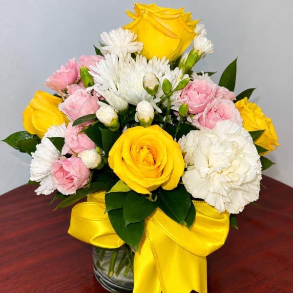 Yellow and pink roses with white daisies in a glass vase with a yellow ribbon