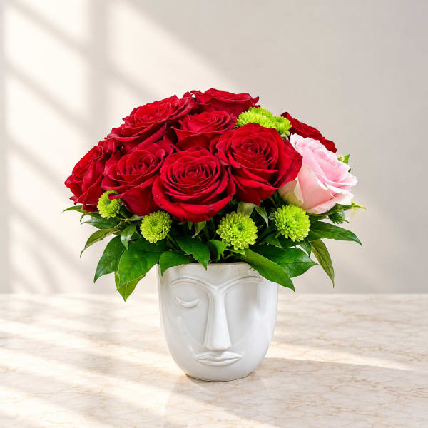Red roses and a pink rose in a white face vase