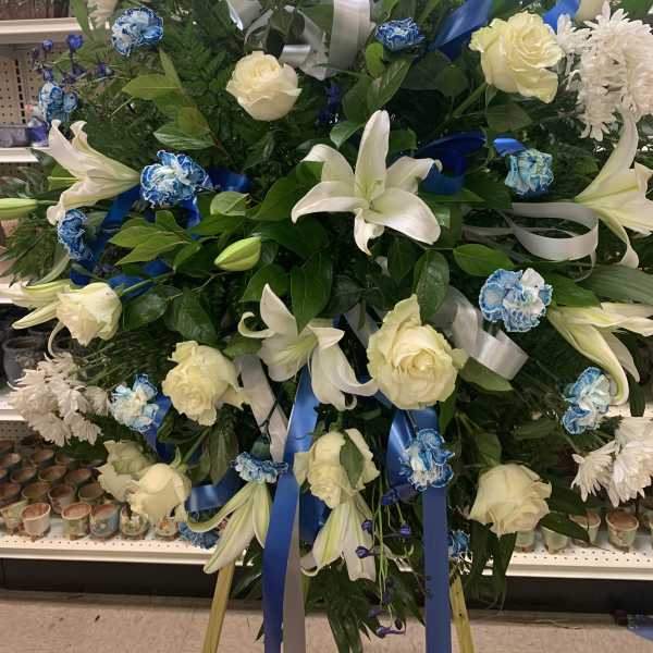 Standing floral spray with white lilies, cream roses, and blue ribbons