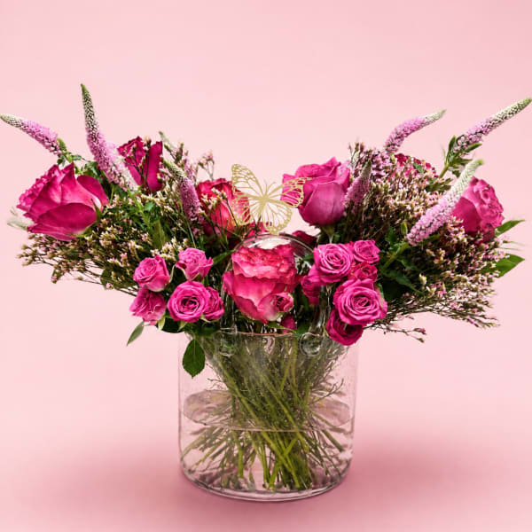 Pink roses and spray roses in a clear glass vase with a butterfly pick