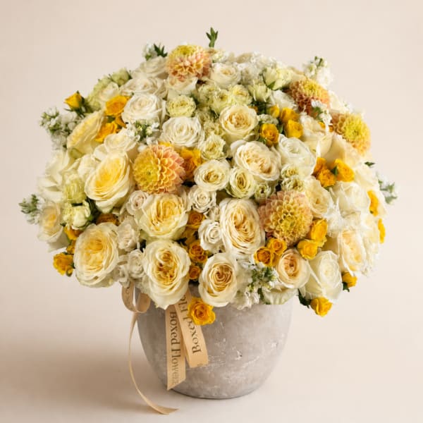 Cream and yellow rose bouquet in a gray vase with a ribbon
