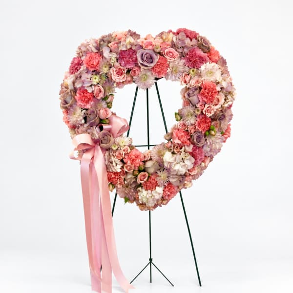 Heart-shaped floral wreath on a stand with pink ribbon