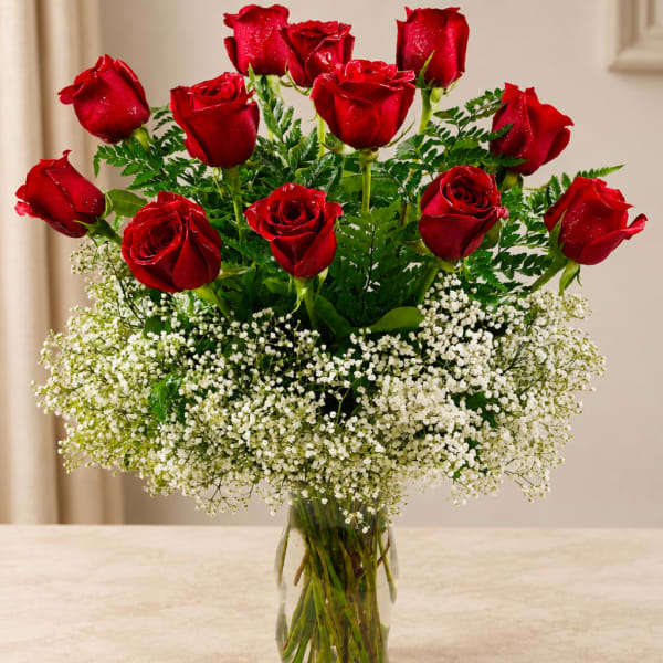 Red roses arranged in a clear glass vase with white baby's breath