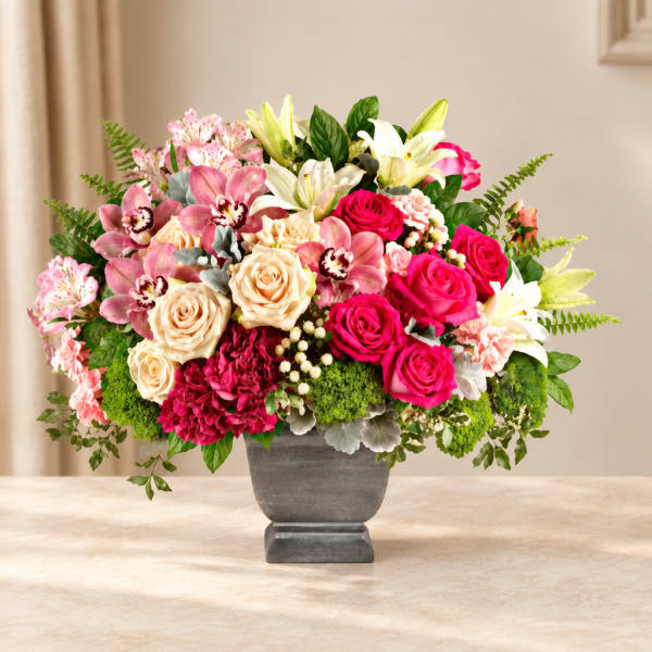 Mixed bouquet of pink roses, lilies, and orchids in a gray vase