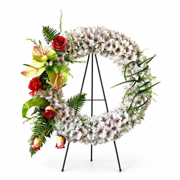 Floral wreath on a black stand with white blooms and red roses