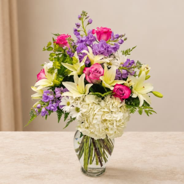 Bouquet of pink roses, white lilies, and purple flowers in a glass vase