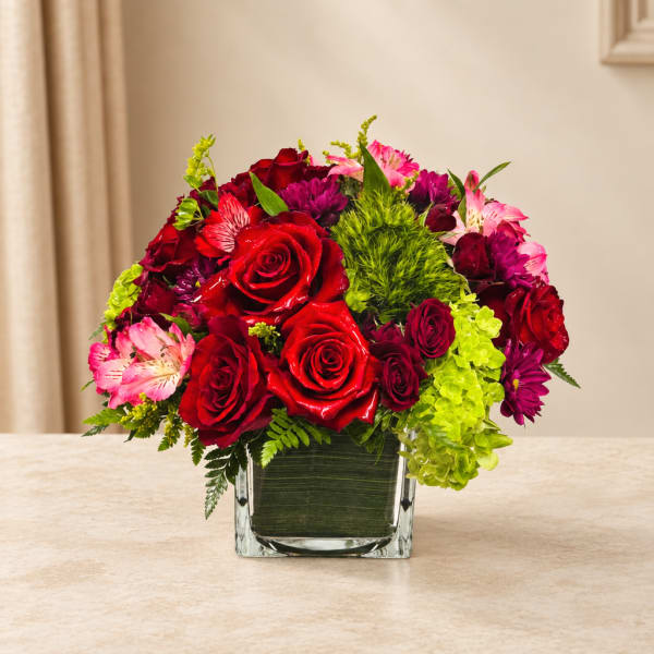 Red roses and pink flowers arranged in a square glass vase