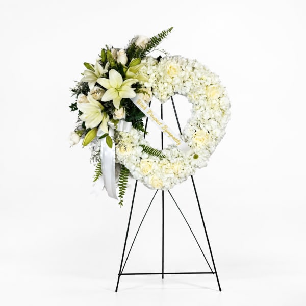 White floral sympathy wreath on a black stand with lilies and roses