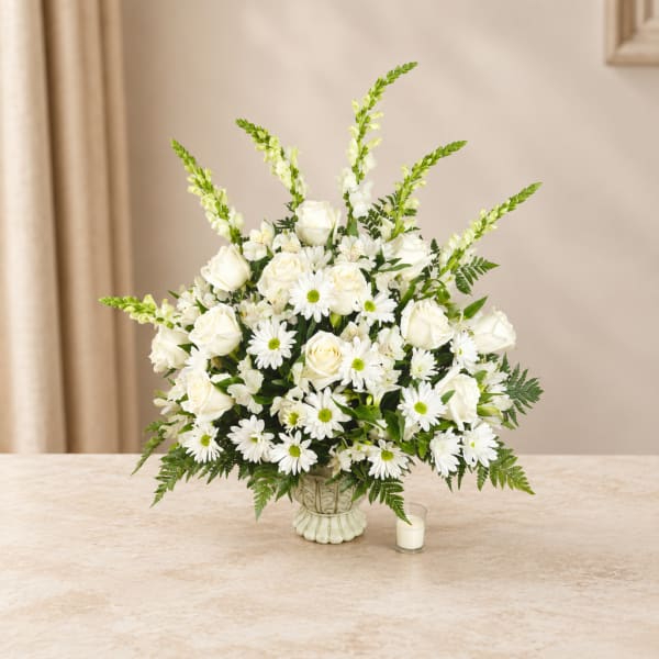 White roses and daisies in a decorative vase with a small candle beside it