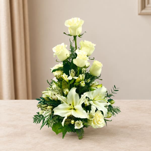 White roses and lilies arranged in a tall vase centerpiece