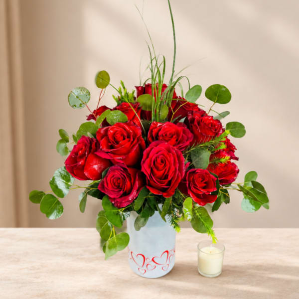 Red roses arranged in a white vase with a small candle beside it