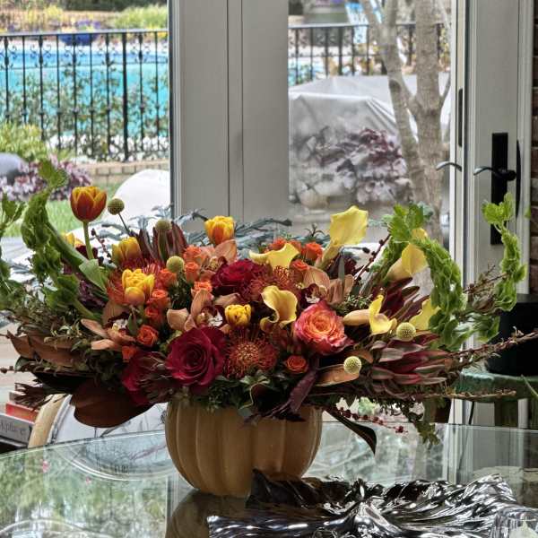 Autumn floral arrangement in a pumpkin-shaped vase with red, orange, and yellow blooms