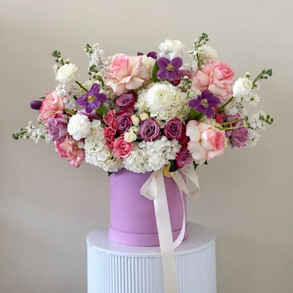 Pink, white, and purple flower arrangement in a lavender hat box with ribbon