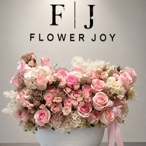 Pink and white rose arrangement in a white bowl vase with a ribbon