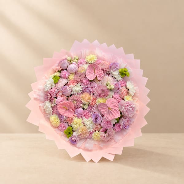 Round bouquet of pink and lavender flowers wrapped in pale pink paper