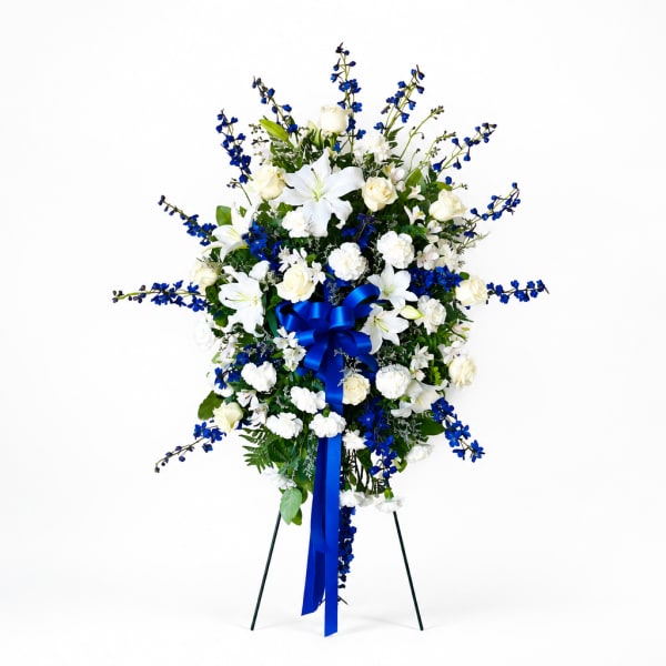 Standing floral spray with white lilies, roses, and blue flowers on a stand