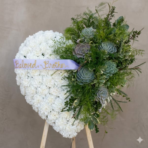 Heart-shaped white floral wreath with green succulents and a lavender ribbon