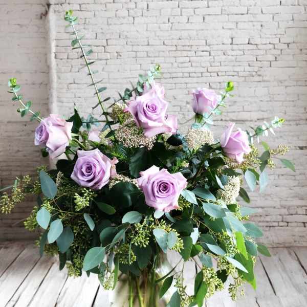 Lavender roses arranged in a glass vase with mixed greenery