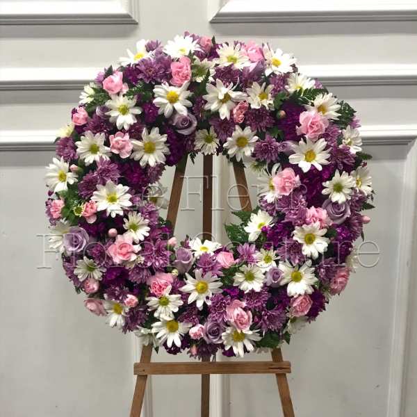 Round floral wreath of pink, purple, and white flowers on a wooden easel