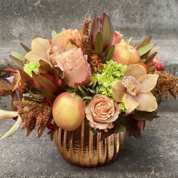 Autumn floral arrangement with peaches and roses in a ribbed glass vase