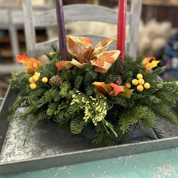 Evergreen centerpiece with fall ribbon, berries, and two taper candles on a metal tray