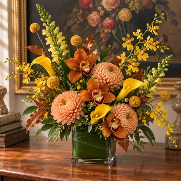 Arrangement of peach mums, yellow calla lilies, and orchids in a glass vase