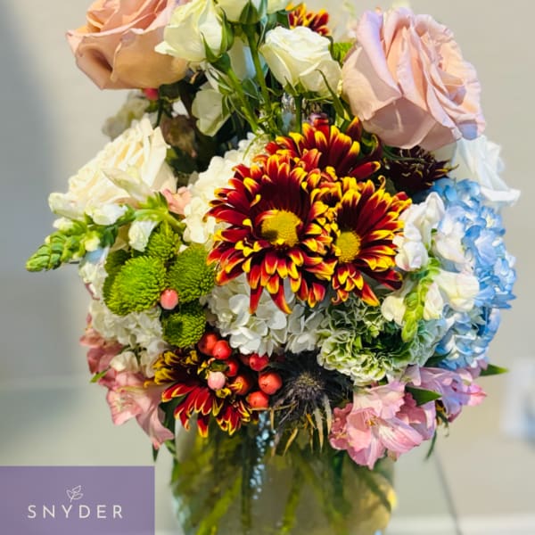 Mixed bouquet of roses, chrysanthemums, hydrangeas, and snapdragons in a glass vase