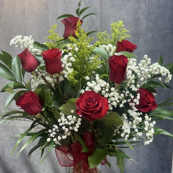 Red roses and white baby's breath in a clear glass vase with a red ribbon