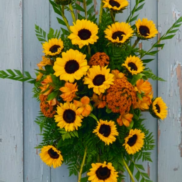 Sunflower and orange floral arrangement with greenery against a blue wood background