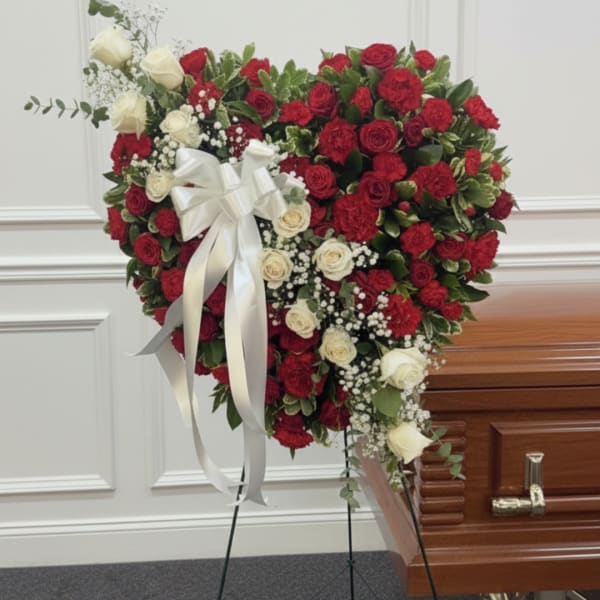 Heart-shaped red and white rose spray on an easel beside a casket