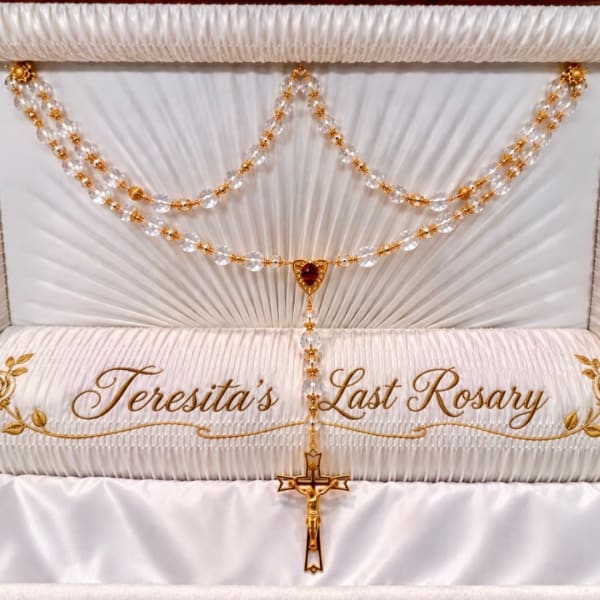 White satin funeral casket with gold rosary and cross