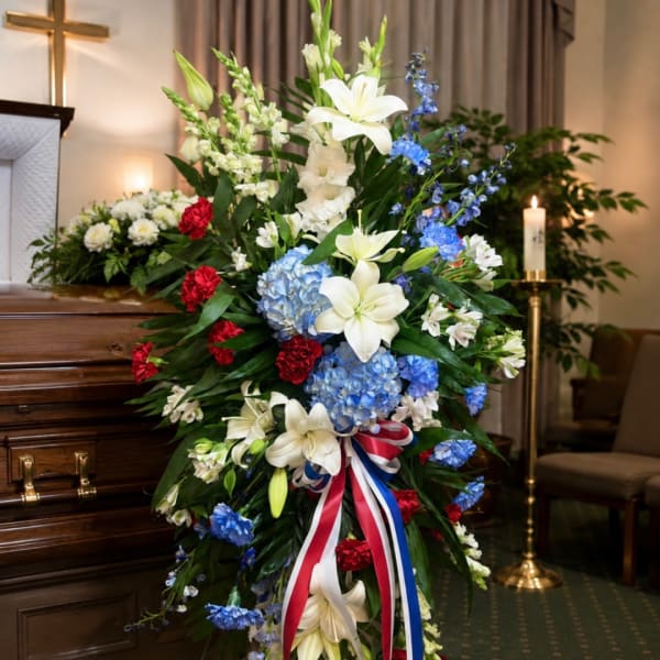 Standing funeral spray with white lilies, blue hydrangeas, and red carnations