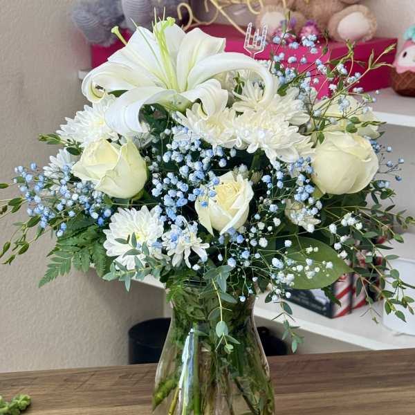 White lilies, roses, and daisies in a glass vase with blue baby's breath