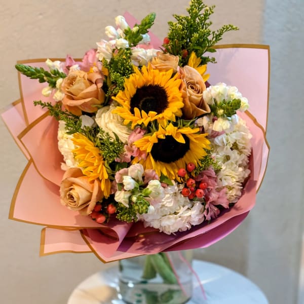 Bouquet of sunflowers, roses, and white blooms wrapped in pink paper