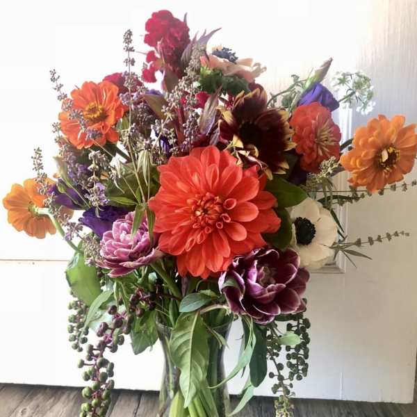 Tall mixed bouquet of orange, red, purple, and white flowers arranged in a clear glass vase.