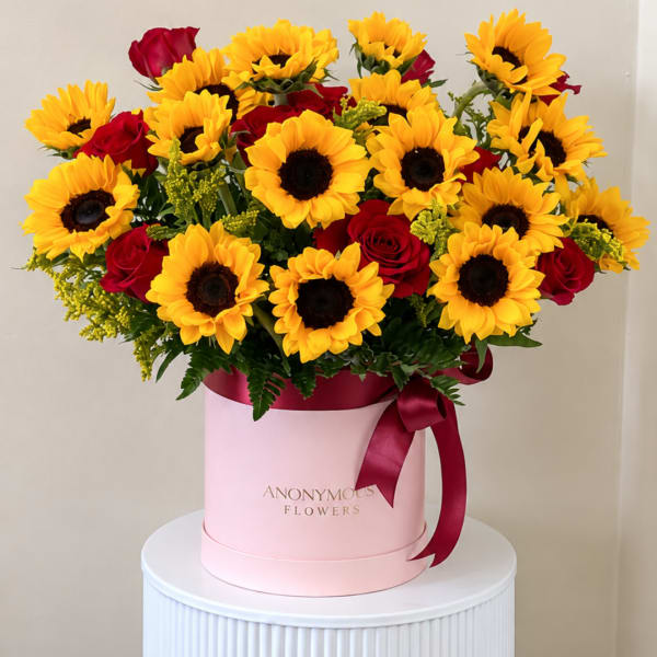 Sunflowers and red roses arranged in a pink hat box with a ribbon