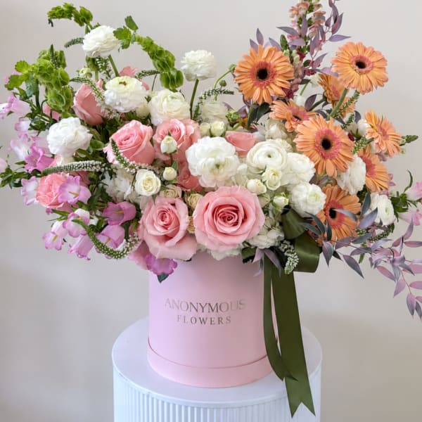 Pink and white mixed bouquet in a pink hatbox with orange daisies