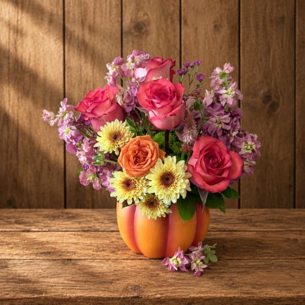 Bouquet of pink and orange roses with yellow daisies in a pumpkin vase