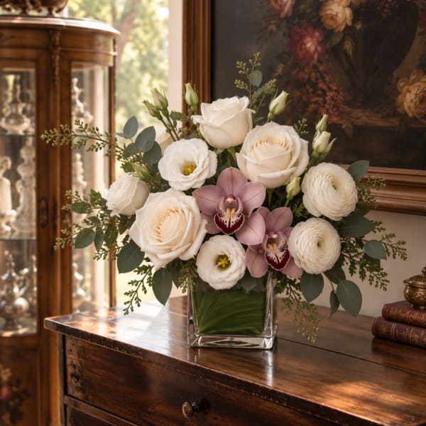White roses and orchids arranged in a clear square vase