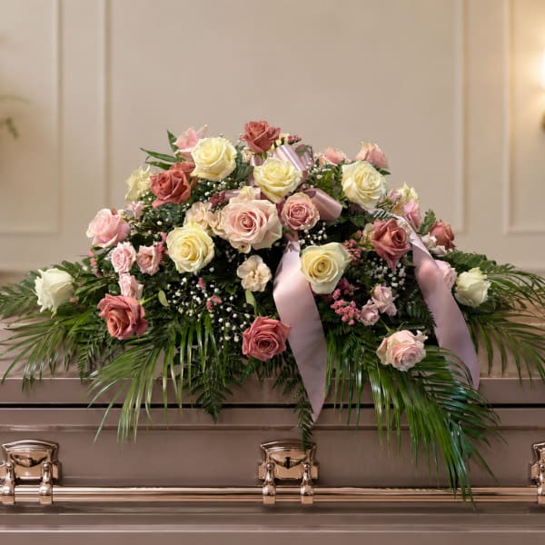 Pastel rose arrangement on a casket with pink ribbon and greenery