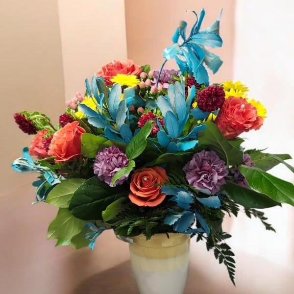 Colorful bouquet of roses, chrysanthemums, and purple blooms in a white vase