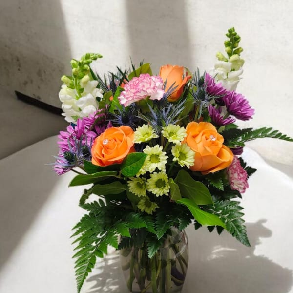 Bouquet of orange roses, purple daisies, and white snapdragons in a glass vase