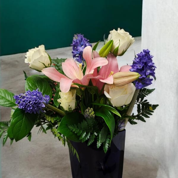 Pink lilies and white roses with purple hyacinths in a black vase